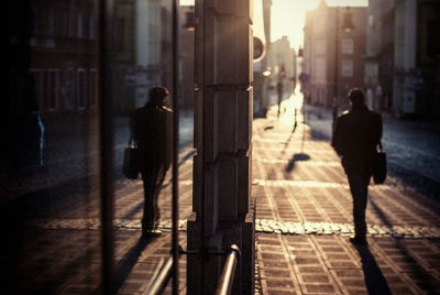 Rear view of man walking on footpath amidst buildings in city