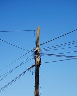 Low angle view of electricity pylon against blue sky