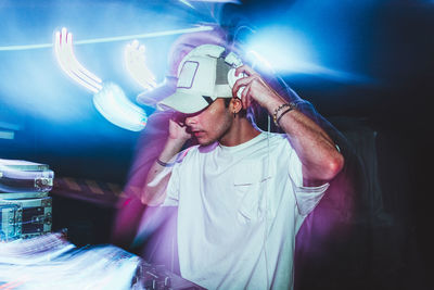 Dj with headphones at night club party under the blue light and people crowd in background