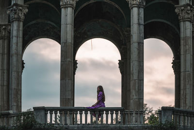 Rear view of woman sitting on fence of an abandoned building 