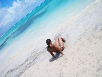 Woman in bikini sitting on shore at beach