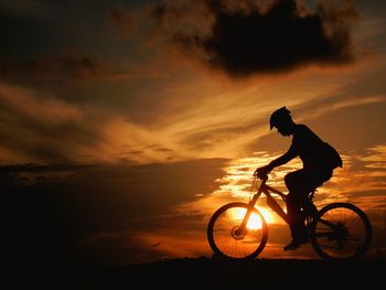Silhouette of man riding bicycle against sky during sunset