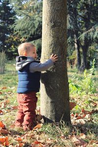 Cute baby boy standing by tree trunk in forest