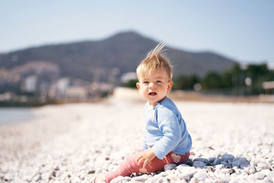 Cute baby boy on pebbles at beach