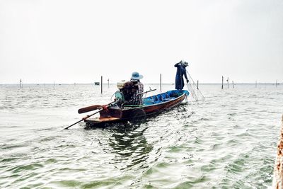 Fishermen on boat on sea against clear sky