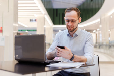 Portrait of young man using mobile phone while sitting in office