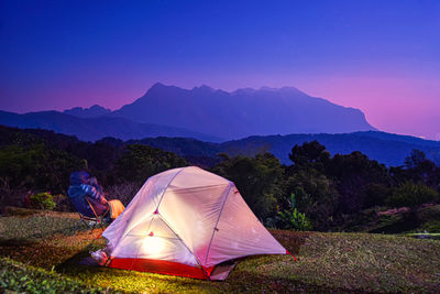 Tent on field by mountains against sky during sunset