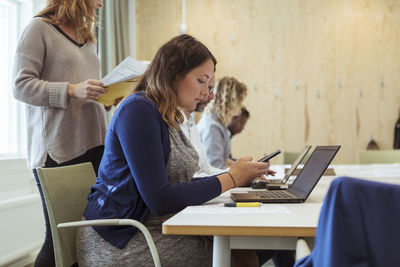 Pregnant businesswoman using mobile phone while sitting at conference table in meeting