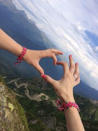 Cropped hands of friends making heart shape against mountains