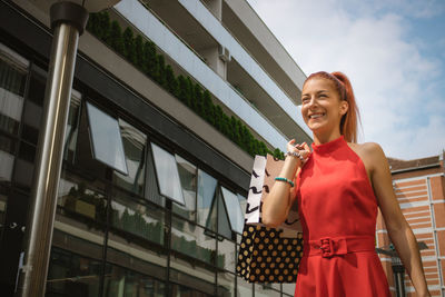 Smiling young woman holding shopping bags while standing by building