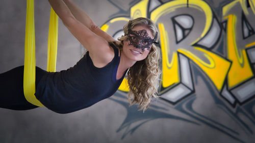 Portrait of woman hanging on silk against graffiti wall