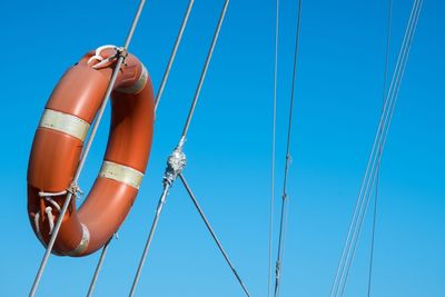 Low angle view of life belt attached to ropes against blue sky