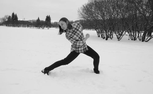 Young woman slipping on snowy field against clear sky