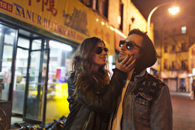 Smiling couple in sunglasses standing at city during night