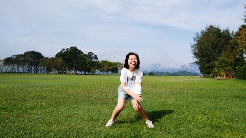 Cheerful woman standing on grassy field against sky