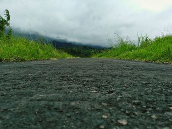 Surface level of road amidst field against sky