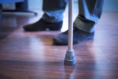 Low section of man with walking cane standing on hardwood floor