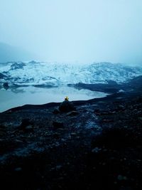 Man sitting on rock against sky during winter