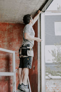 A young caucasian man repairing a window opening while standing on a metal stepladder