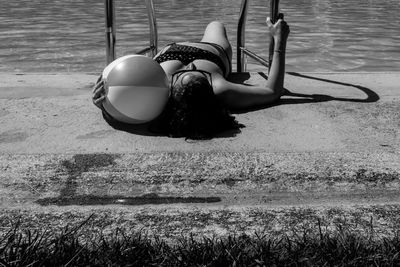 Bikini woman with beach ball lying at poolside during sunny day