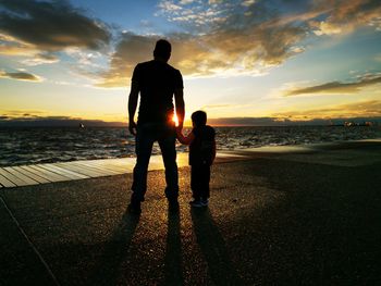 Rear view of man standing at beach against sky during sunset