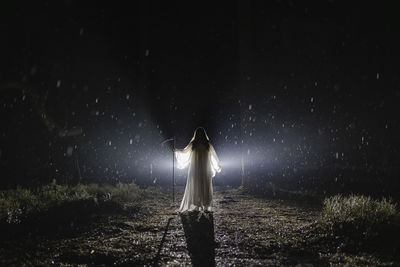 Ghost with scythe standing in forest at night during rainy season