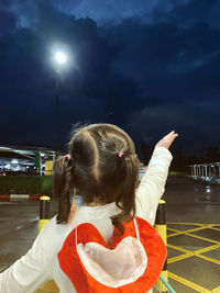 Rear view of girl standing against illuminated sky