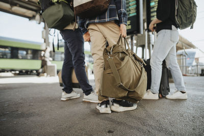 Low section of boy holding luggage while standing with family at railroad station