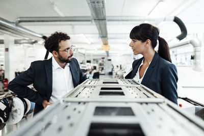 Confident colleagues discussing while standing by machinery at industry