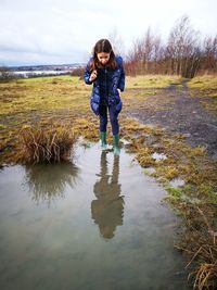 Full length of girl standing on grass and puddle against sky