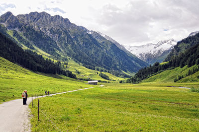 People on footpath amidst green mountains against sky