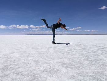 Full length of man balancing at salar de uyuni against blue sky on sunny day