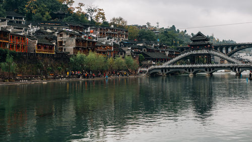 Bridge over river by buildings in town against sky