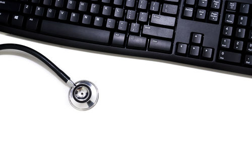 Close-up of computer keyboard and stethoscope over white background