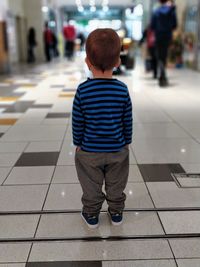 Rear view of boy standing on tiled floor at airport