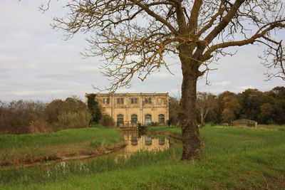 Old building by trees on field against sky