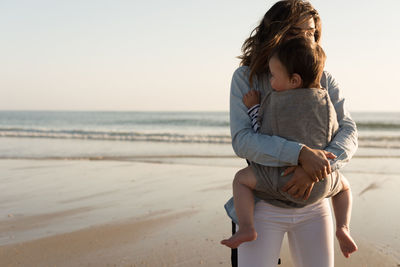 Mother carrying son while standing at beach