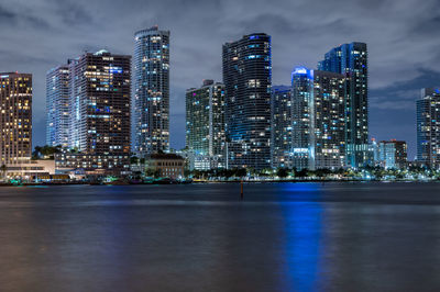 Illuminated modern buildings in city against sky at night