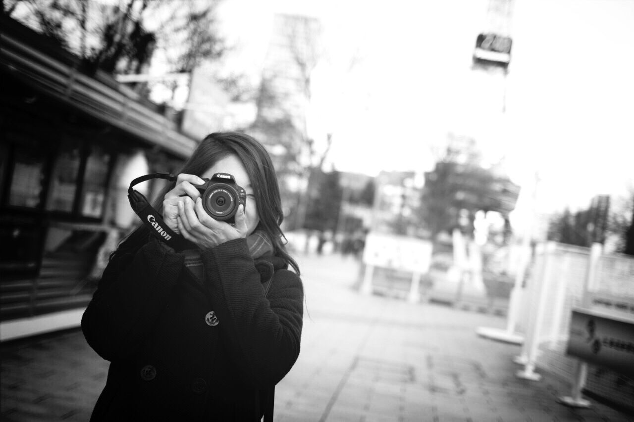 PORTRAIT OF YOUNG WOMAN STANDING BY STREET