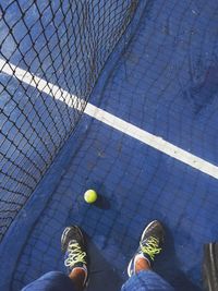 Low section of man standing by net and ball on blue tennis court