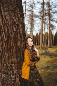 Portrait of beautiful young woman. she is leaning on tree in the forest. eyes closed