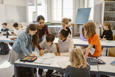 Female teacher assisting students learning together in classroom