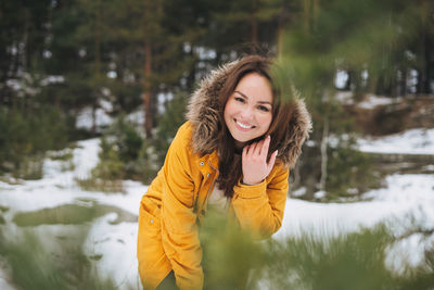 Portrait of young smiling beautiful woman in yellow jacket walking in winter forest