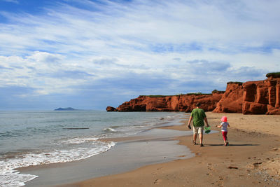 Man with daughter walking at beach against sky