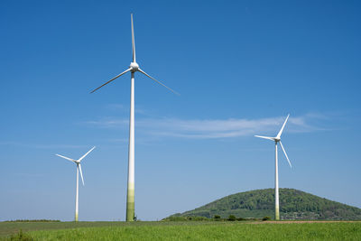 Windmills on field against clear blue sky