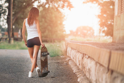 Rear view of woman with skateboard standing on footpath