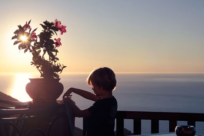 Boy looking at sea against sky during sunset