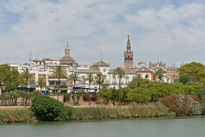 View of buildings by river against cloudy sky