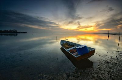 Boat moored on shore against sky during sunset