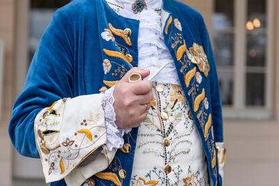 The details of man dressed in a baroque costume. a hand holding a pipe, golden buttons, vest.
